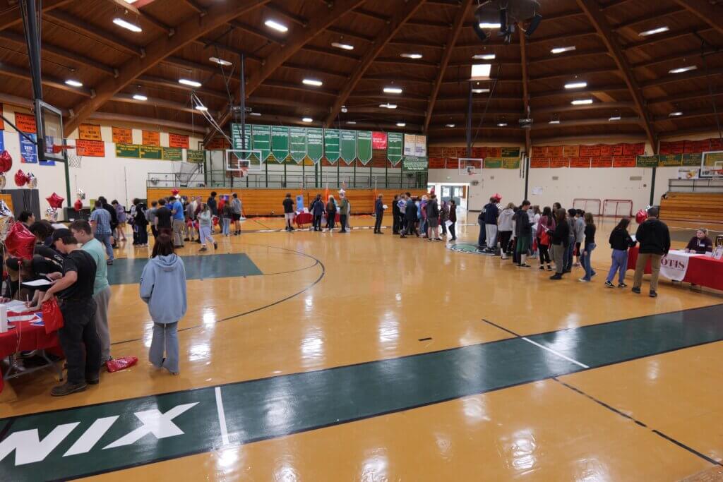 Birds eye view of gymnasium full of students standing at various booths.