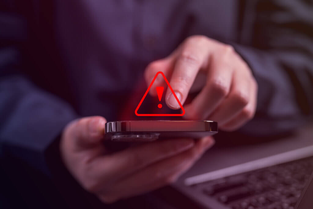 Hands holding cell phone with caution symbol above.